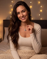 Brunette woman in a cozy fairy-lit bedroom touching her I love you to the moon and back heart pendant necklace