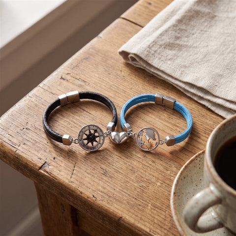 Matching his-and-hers compass bracelets with magnetic half-hearts clicked together on a wooden table