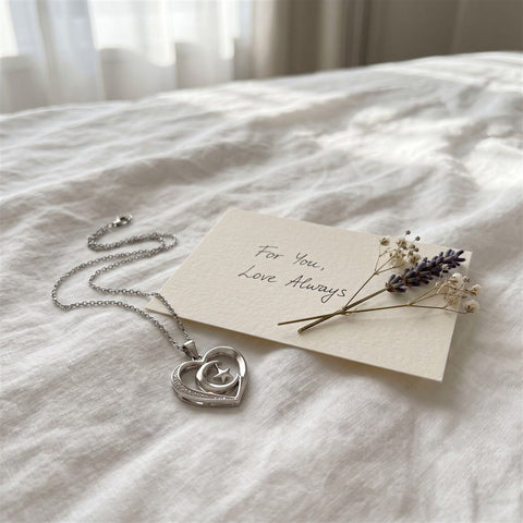 Silver heart necklace with star and moon pendant on bed linen with a handwritten card