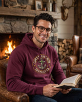 Man with glasses in a maroon Lucky Anchor crest hoodie reading by a stone fireplace