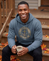 Smiling man in a slate blue Lucky Anchor crest hoodie on autumn porch steps with a coffee
