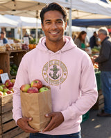 Smiling man in a light pink Lucky Anchor crest hoodie holding apples at a farmers market