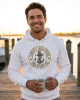 Smiling man in a white Lucky Anchor crest hoodie holding a coffee on a dock at sunrise