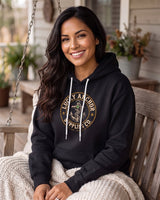 Smiling woman in a black Lucky Anchor crest hoodie wrapped in a blanket on a porch swing