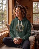 Smiling woman in a forest green Lucky Anchor crest hoodie holding a mug on a cabin window seat