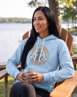 Smiling woman in a light blue Lucky Anchor crest hoodie in an Adirondack chair on a lakeside porch