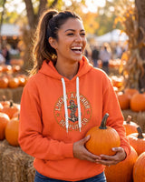 Laughing woman in an orange Lucky Anchor crest hoodie holding a pumpkin at a pumpkin patch