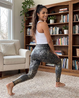 Woman lunging in black metallic woven leggings in front of a bookcase, side view